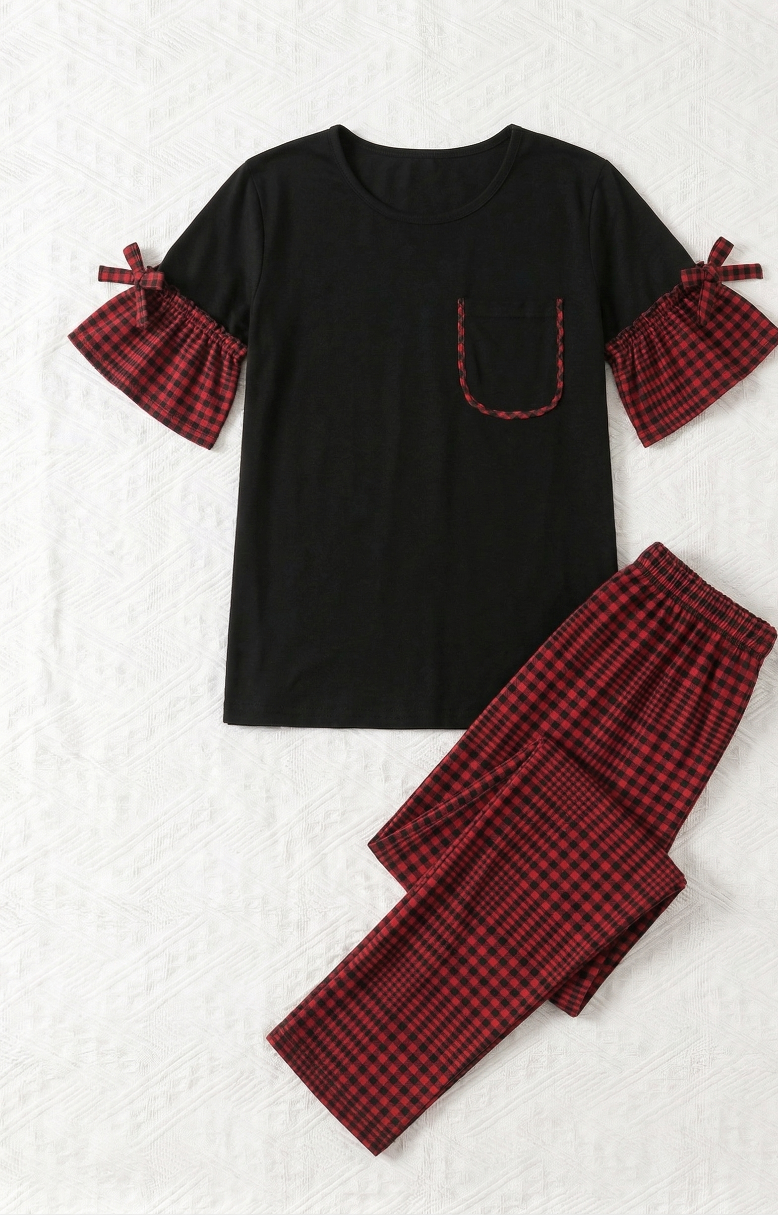 Black top with red plaid sleeves and matching pants on a textured white background